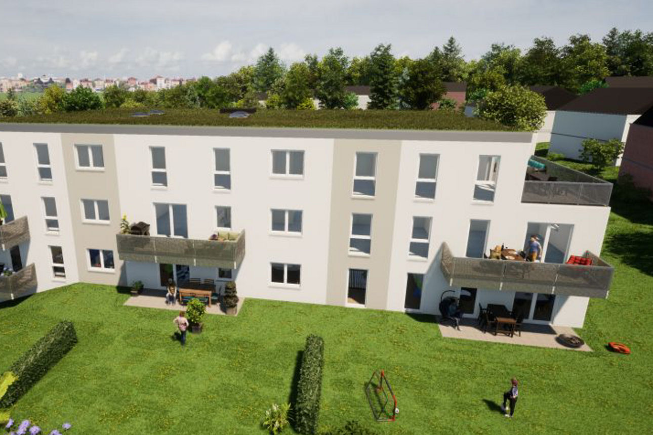 Mehrstöckiges Wohngebäude mit Balkonen und begrüntem Dach, umgeben von einer großen Rasenfläche mit Sträuchern.