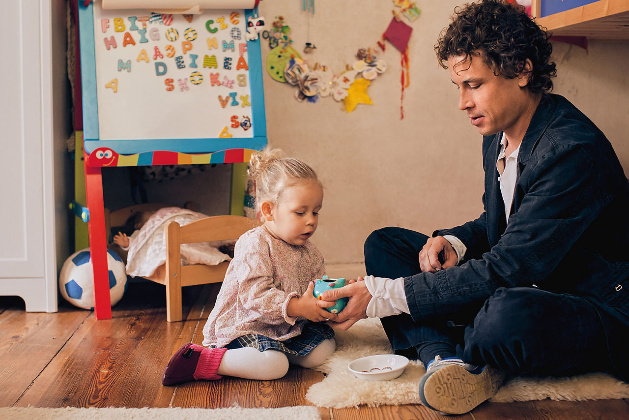 Vater und Kleinkind sitzen am Boden eines Kinderzimmers und spielen