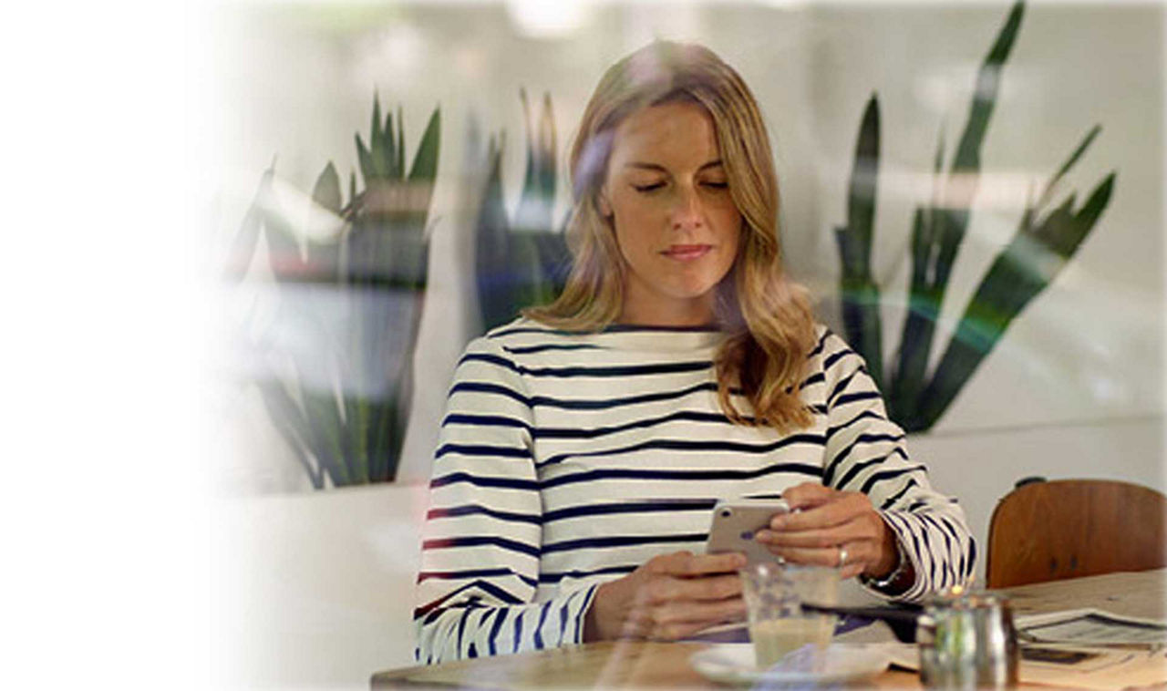 Eine Frau sitzt am Esstisch und schaut auf ihr Handy