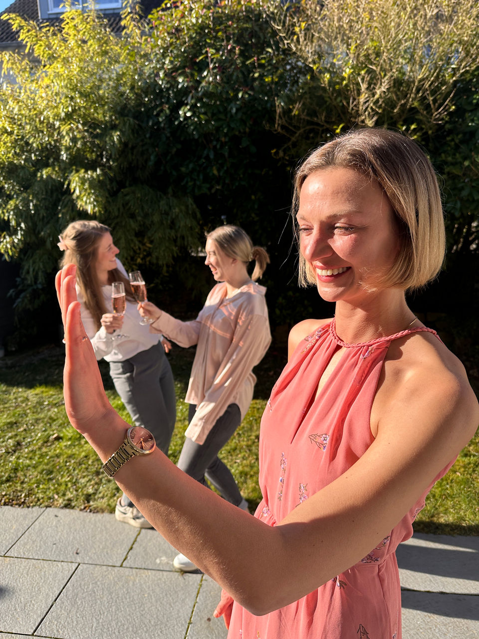 Hanna kann "Ja" sagen: Frau, die ihren Ring betrachtet, im Hintergrund zwei Frauen, die mit Sekt darauf anstoßen