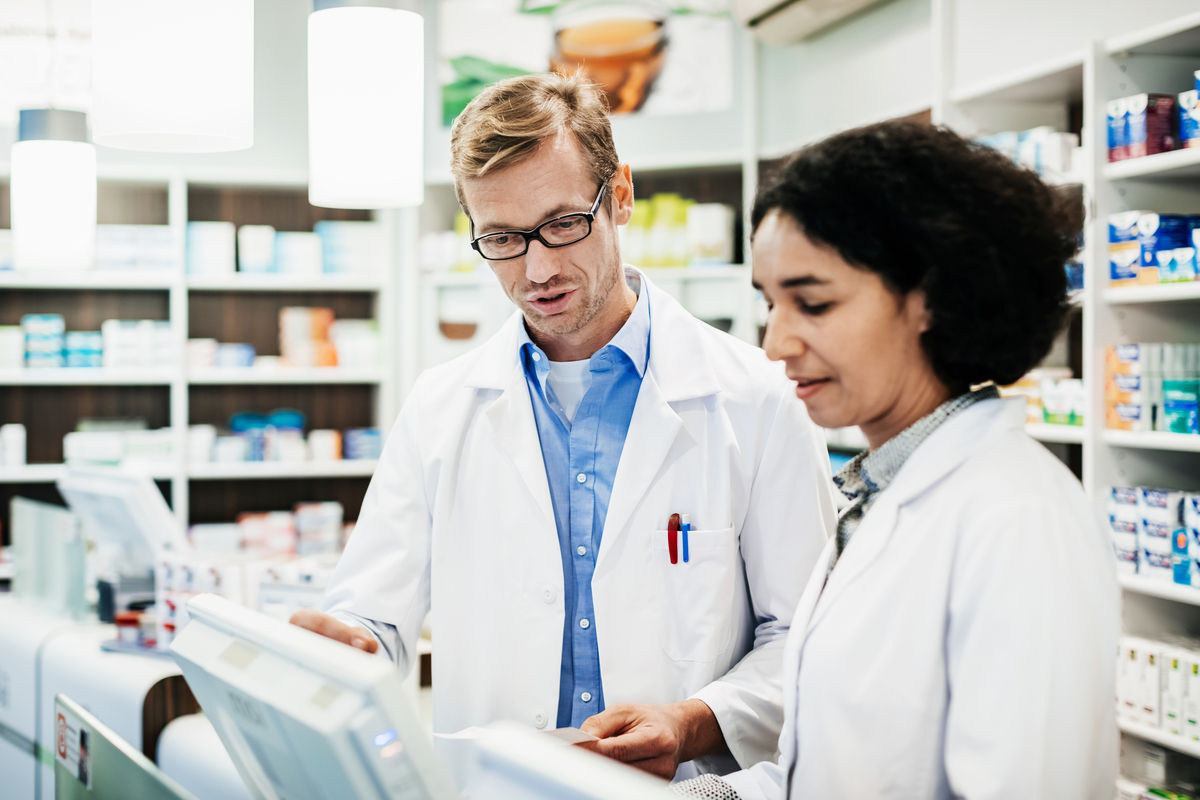 Two pharmacists behind the counter, looking at a computer and talking about a customer's prescription.