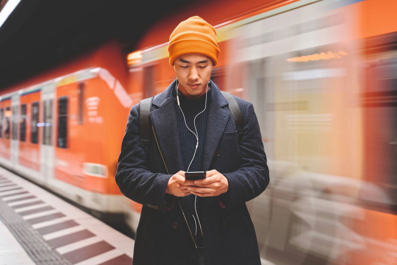 Ein Mann schaut auf sein Handy und steht vor einem Zug