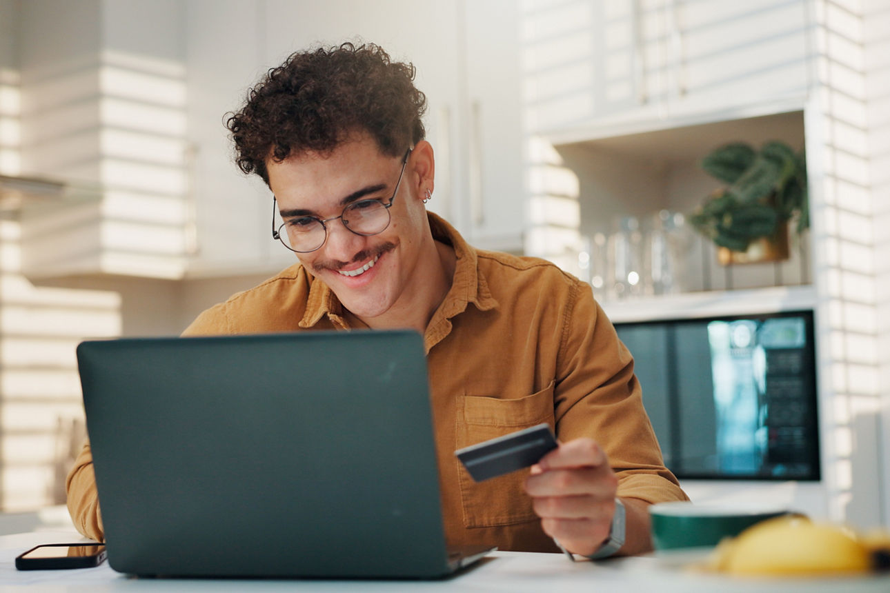 Junger Mann mit Kreditkarte mit Laptop zu Hause beim banking.