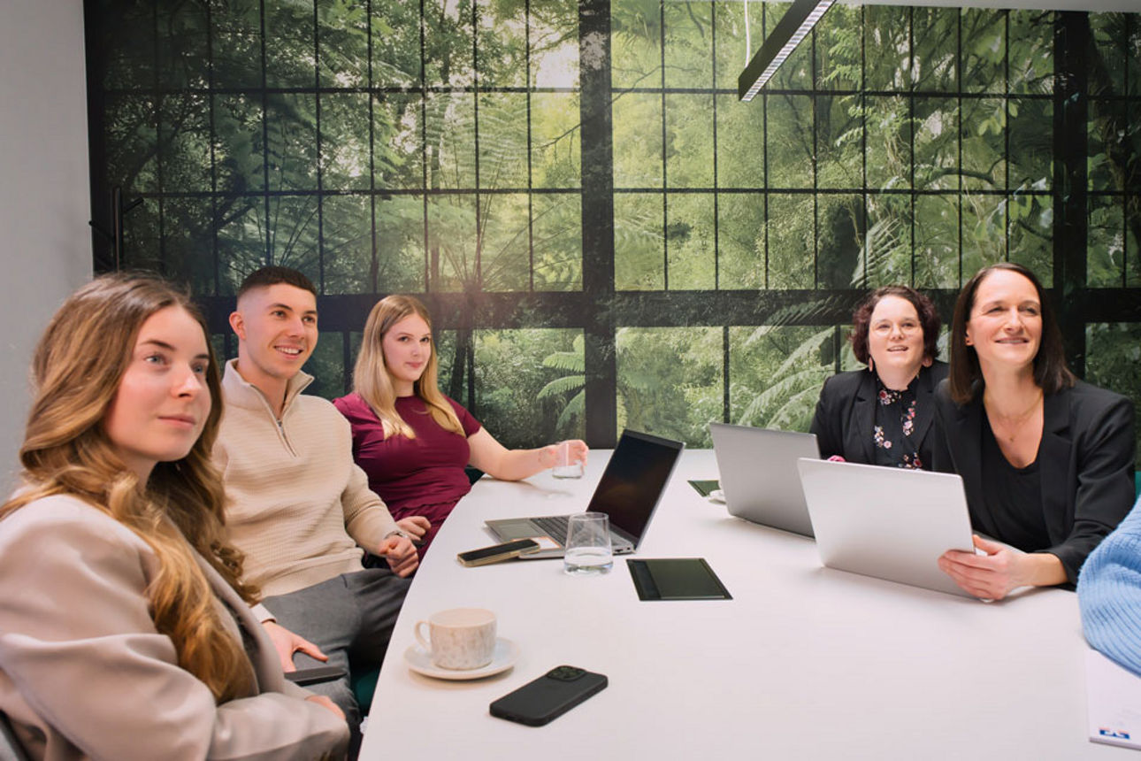 Teammeeting mit fünf Personen am Schreibtisch in einer Bank