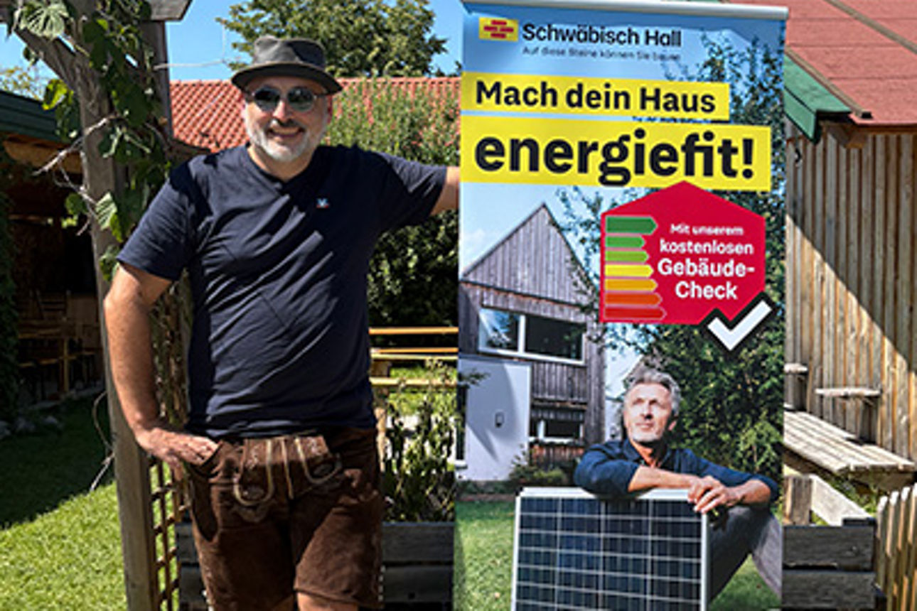 Ein Mann steht vor einem Rollup und lacht.