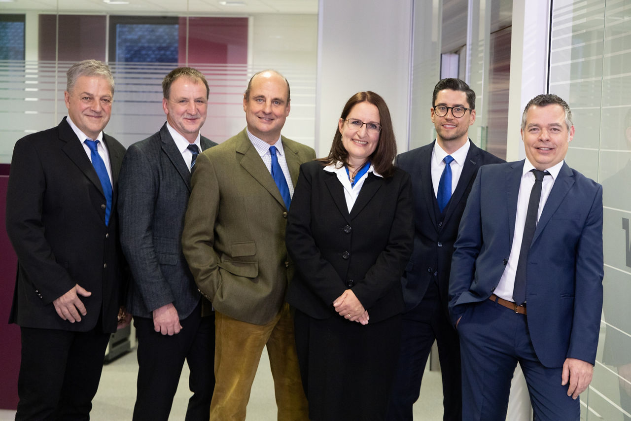 Eine Gruppe von Geschäftsleuten in Anzügen und Krawatten, die in einem Unternehmensumfeld eine Diskussion führen.  