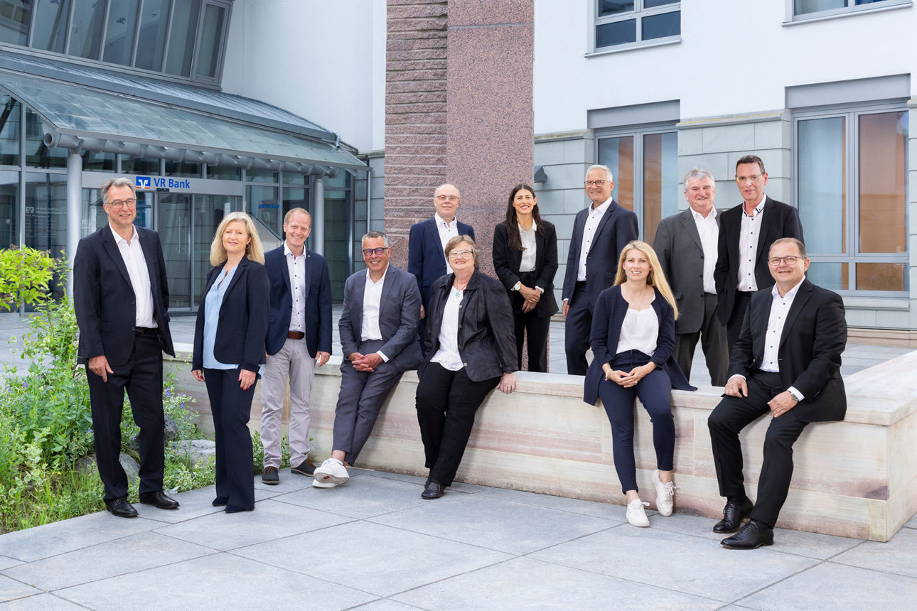 Zehn Personen in Businesskleidung posieren vor einem modernen Gebäude.