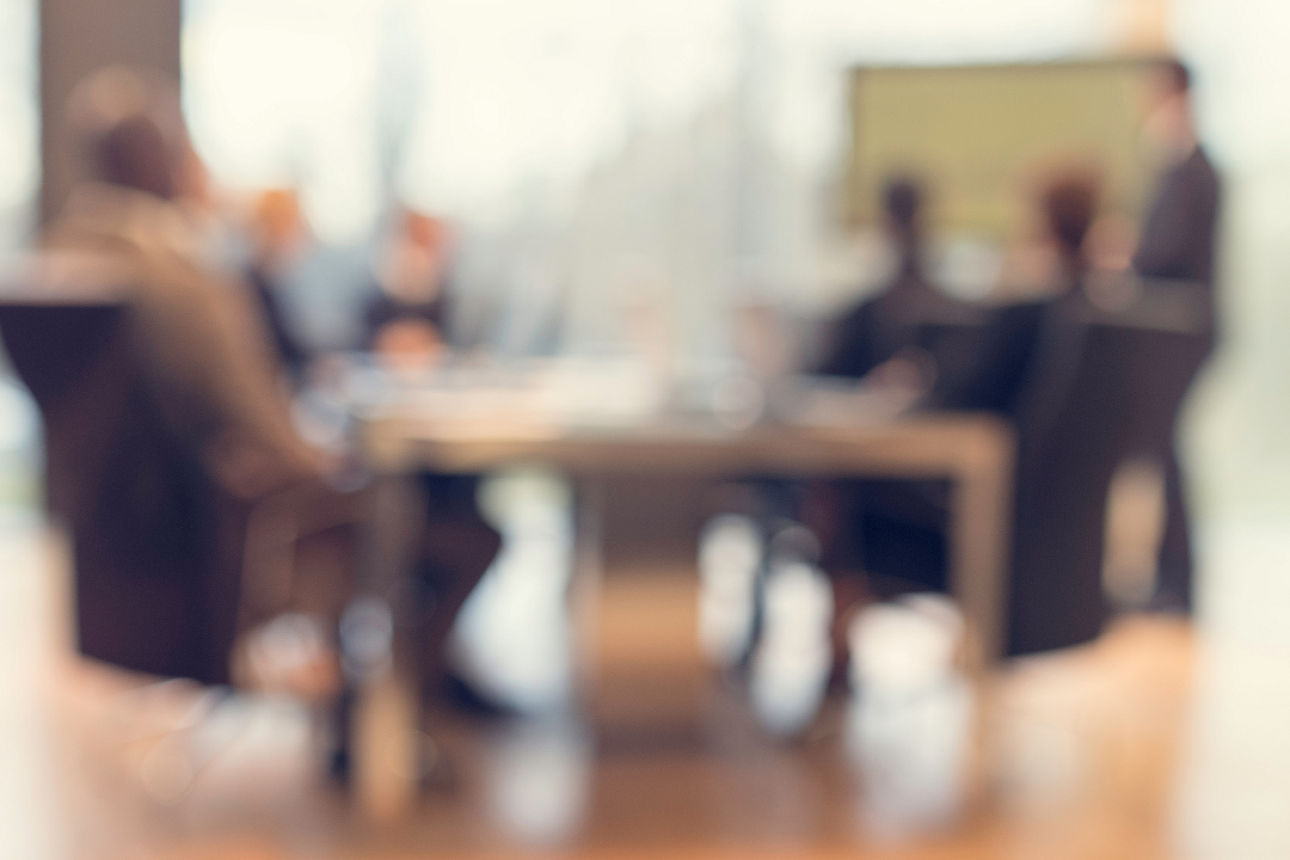 Mehrere Personen sitzen unscharf an einem Konferenztisch in einem modernen Büro bei einer Finanzbesprechung.