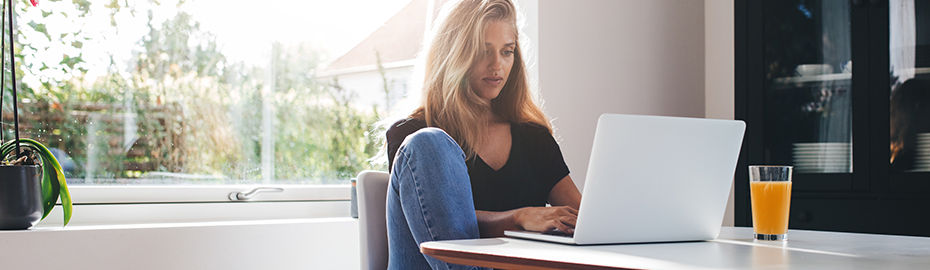 Frau sitzt am Tisch mit Laptop in der Küche