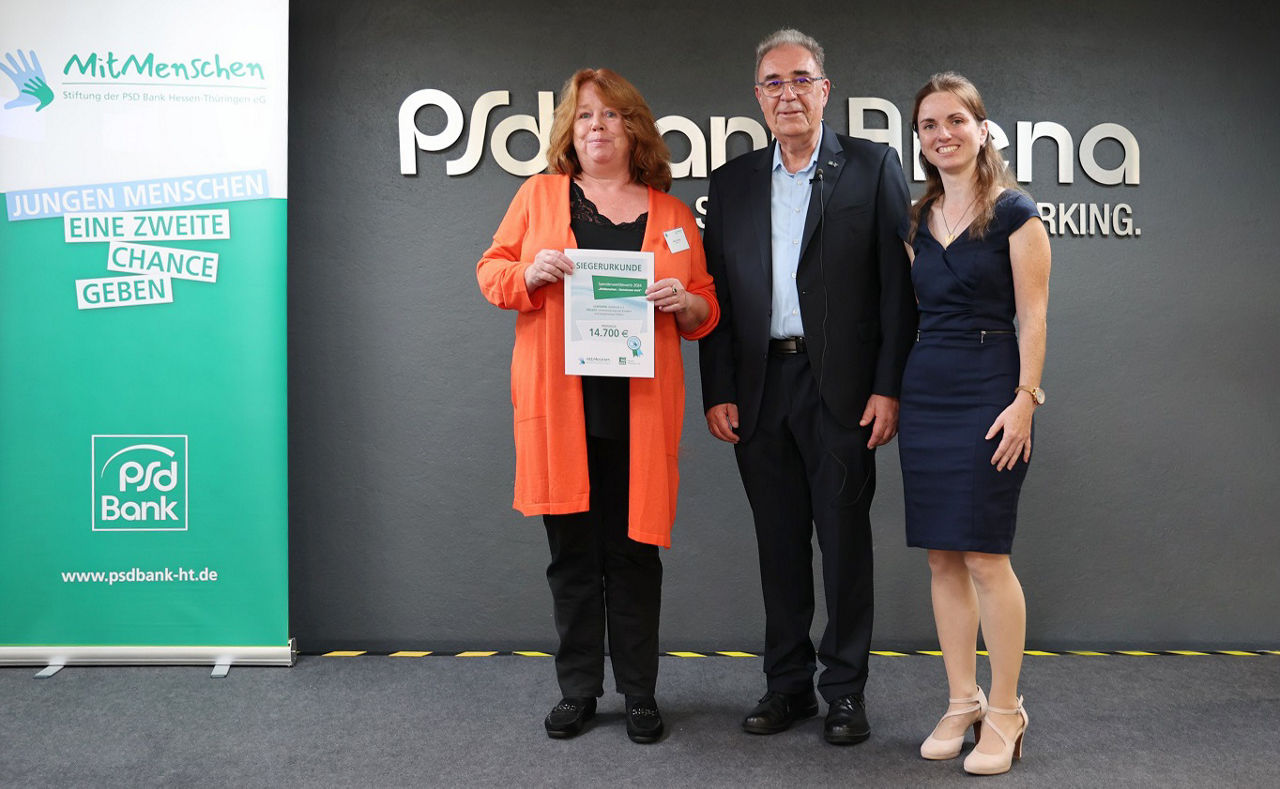 Zwei Frauen und ein Mann stehen vor PSD Wand, Frau hält Siegerurkunde in der Hand
