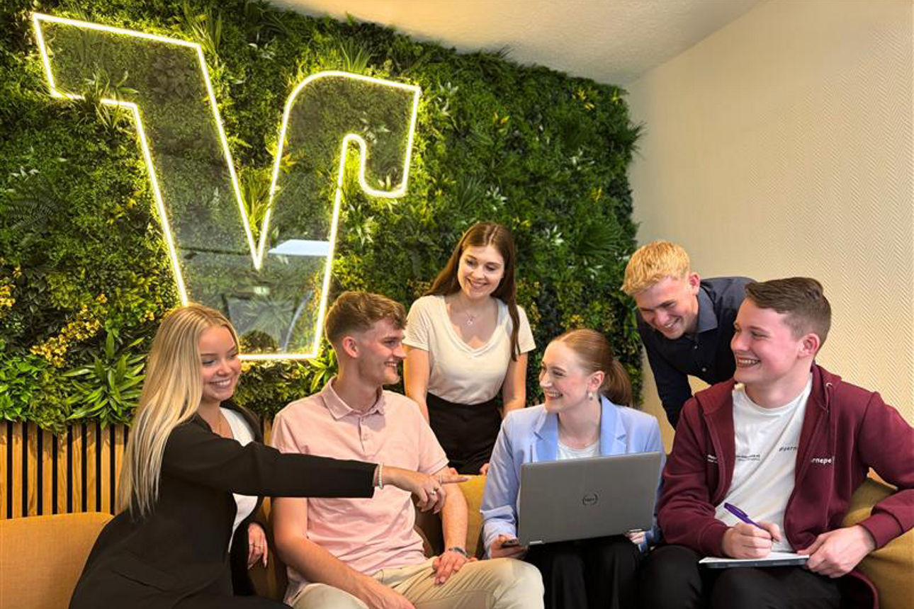 Sechs Auszubildende schauen lachend auf ein Laptop