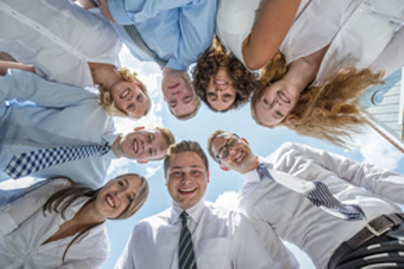 8 junge Leute in Bankkleidung schauen im Kreis nach unten in die Kamera