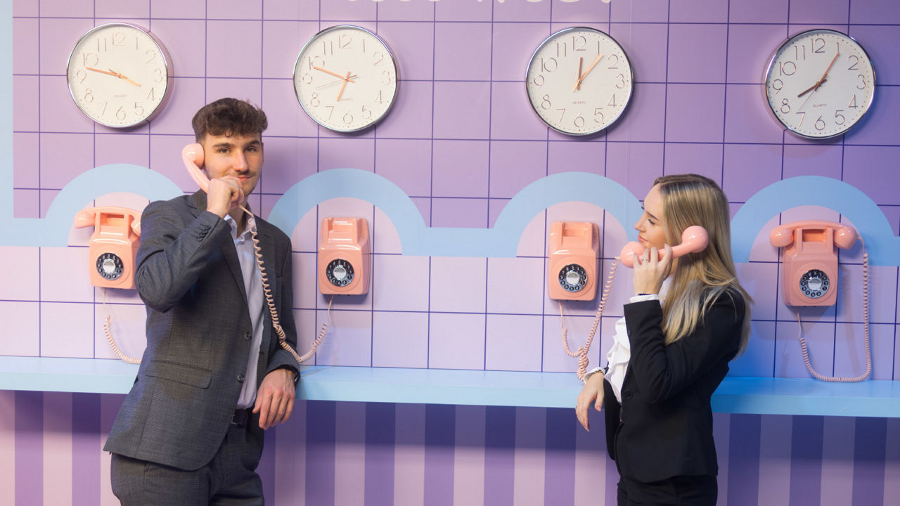 Ein junger Mann und eine junge Frau stehen halten einen alten Retro Telefonhörer ans Ohr. 
