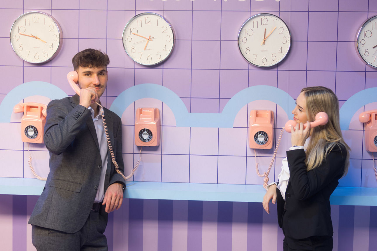 Ein junger Mann und eine junge Frau stehen halten einen alten Retro Telefonhörer ans Ohr. 