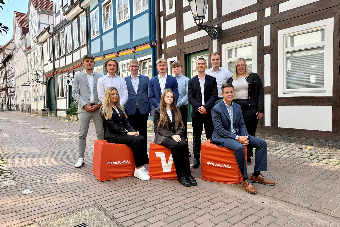 Eine Gruppe von Auszubildenden der Volksbank Hameln-Stadthagen posiert vor einer historischen Fachwerkhäuserkulisse. 
