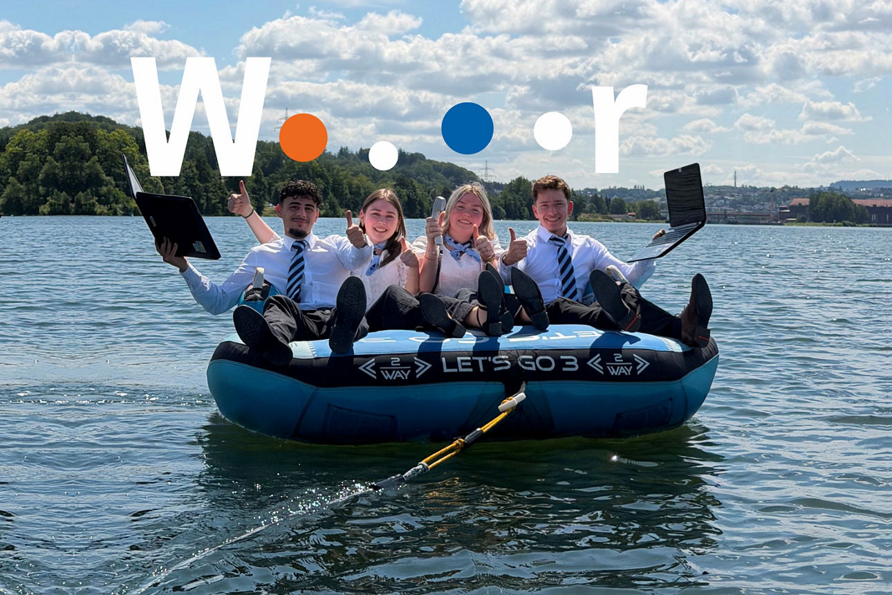 Vier Bankauszubildende mit Laptop und Telefon auf Luftkissen in der Donau, über Ihnen das Wort „Wir“.