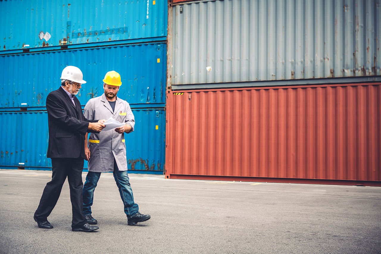 Zwei Männer laufen vor Containern am Hafen