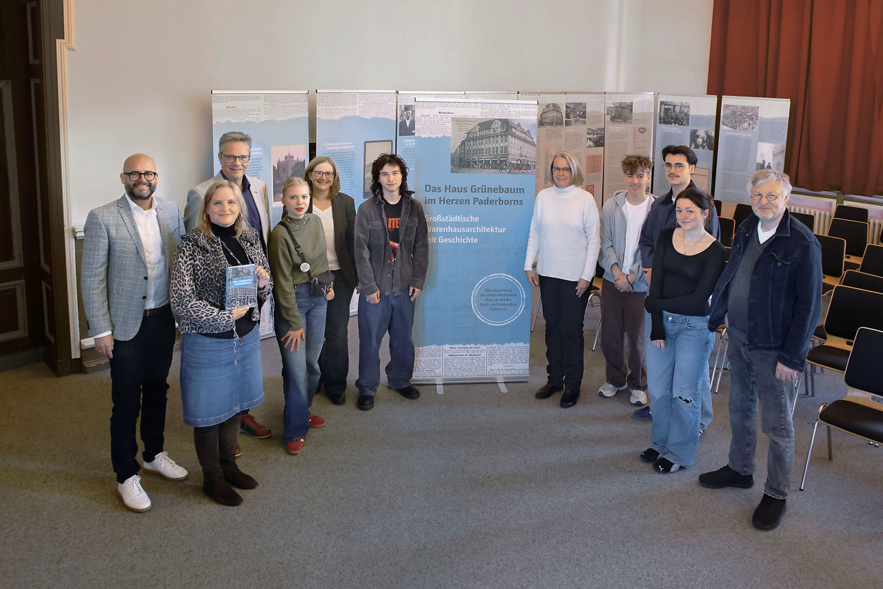 An der Ausstellung beteiligte Personen stehen in der Aula einer Schule