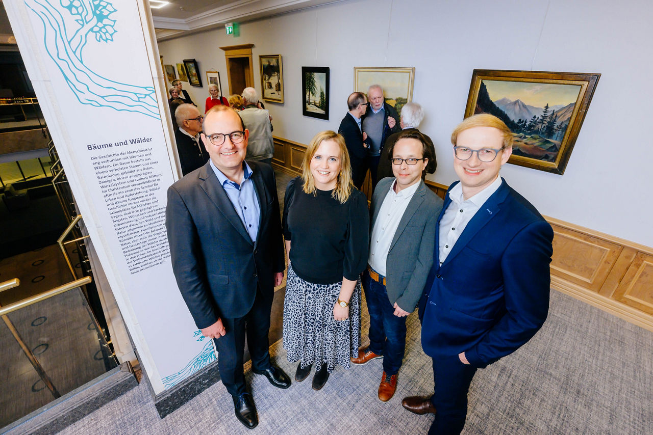 An der Ausstellung beteiligte Personen stehen vor den Kunstwerken. 