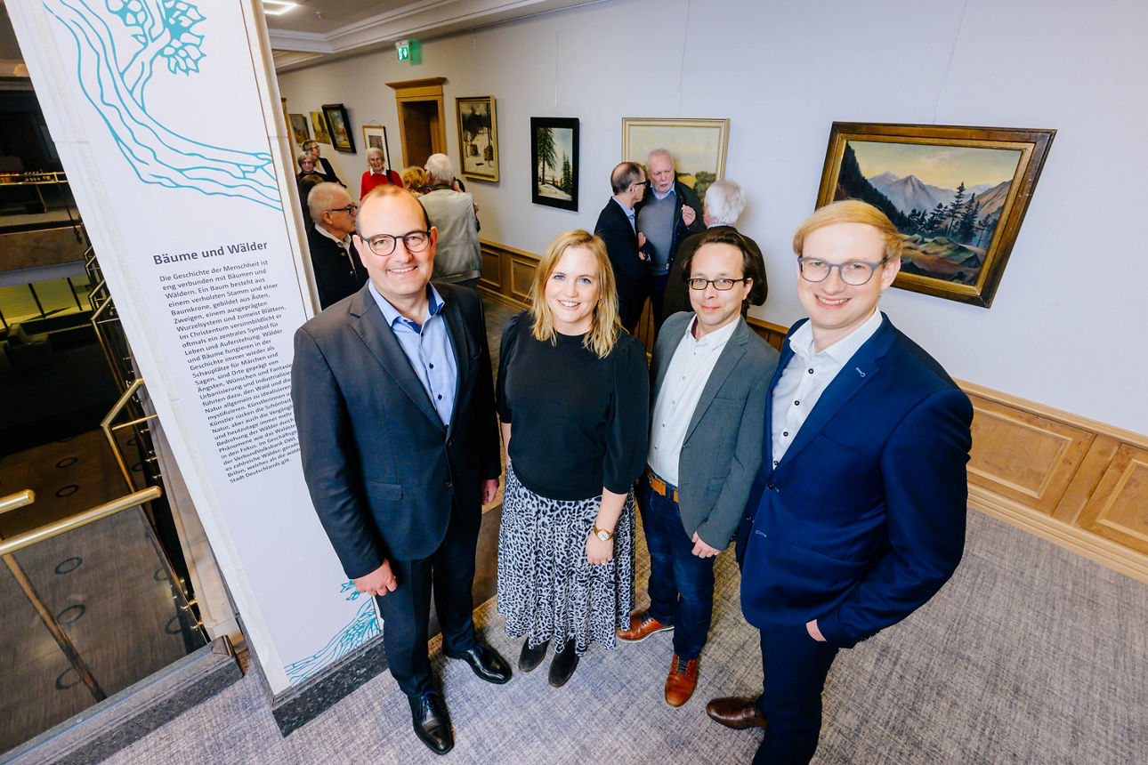 An der Ausstellung beteiligte Personen stehen vor den Kunstwerken. 