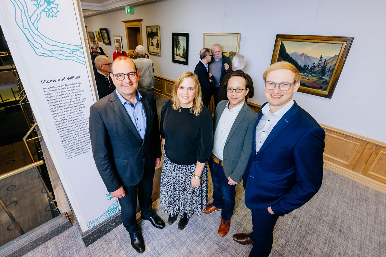 An der Ausstellung beteiligte Personen stehen vor den Kunstwerken. 