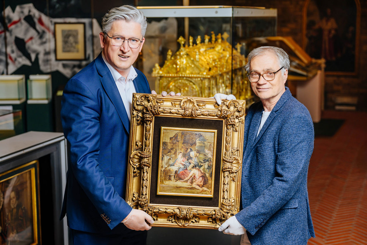 Zwei Männer halten ein Gemälde in der Hand.
