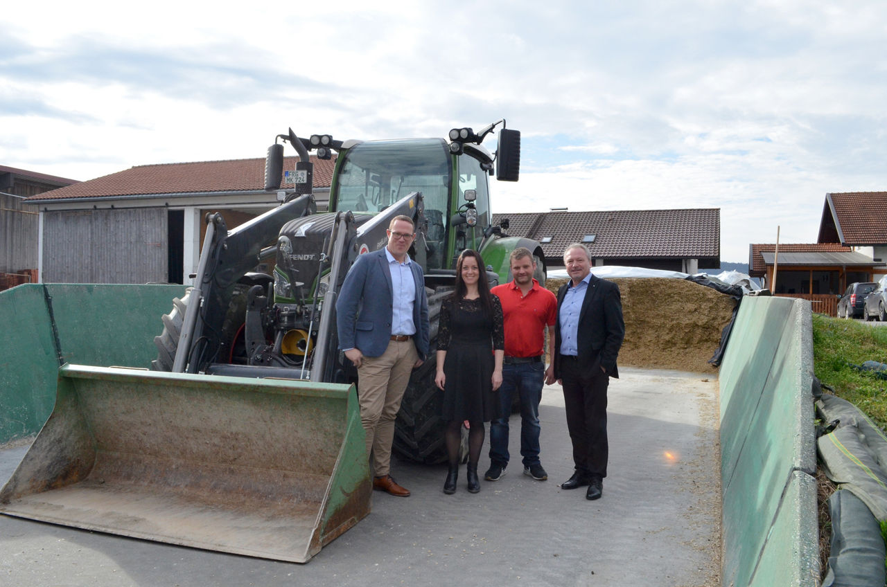 drei Herren und eine Dame stehen vor einem Traktor auf einem landwirtschaftlichen Anwesen