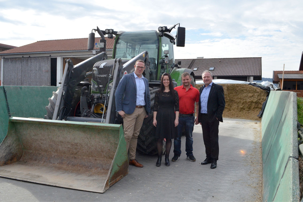 vier Personen vor einem grünen Traktor