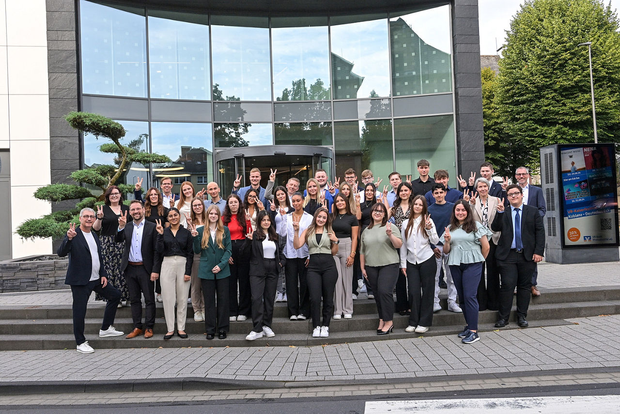 Viele Personen stehen vor einem Bankgebäude zu einem Gruppenbild zusammen.