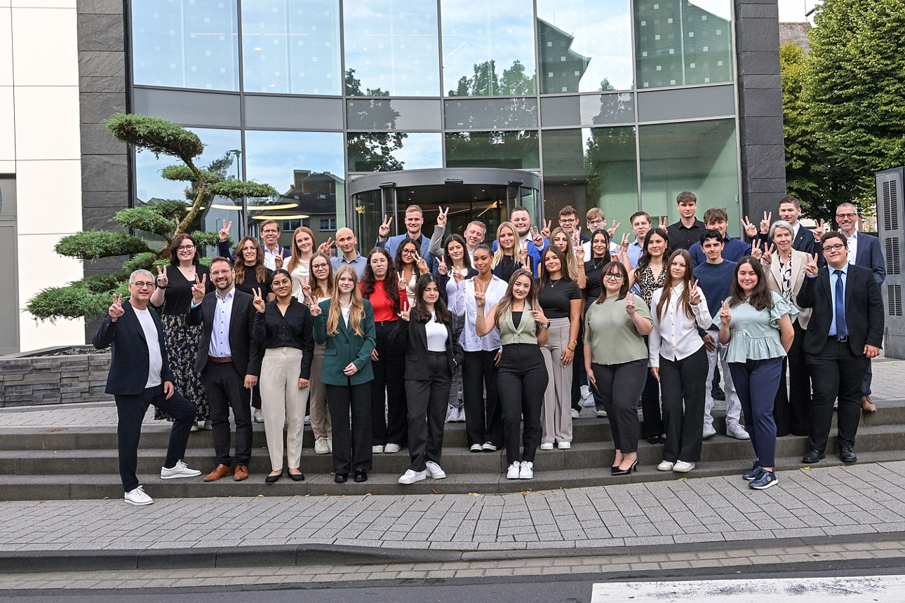 Viele Personen stehen vor einem Bankgebäude zu einem Gruppenbild zusammen.