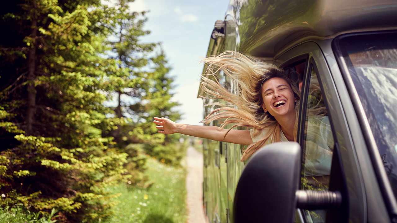Frau lehnt sich lachend während der Fahrt aus dem Auto
