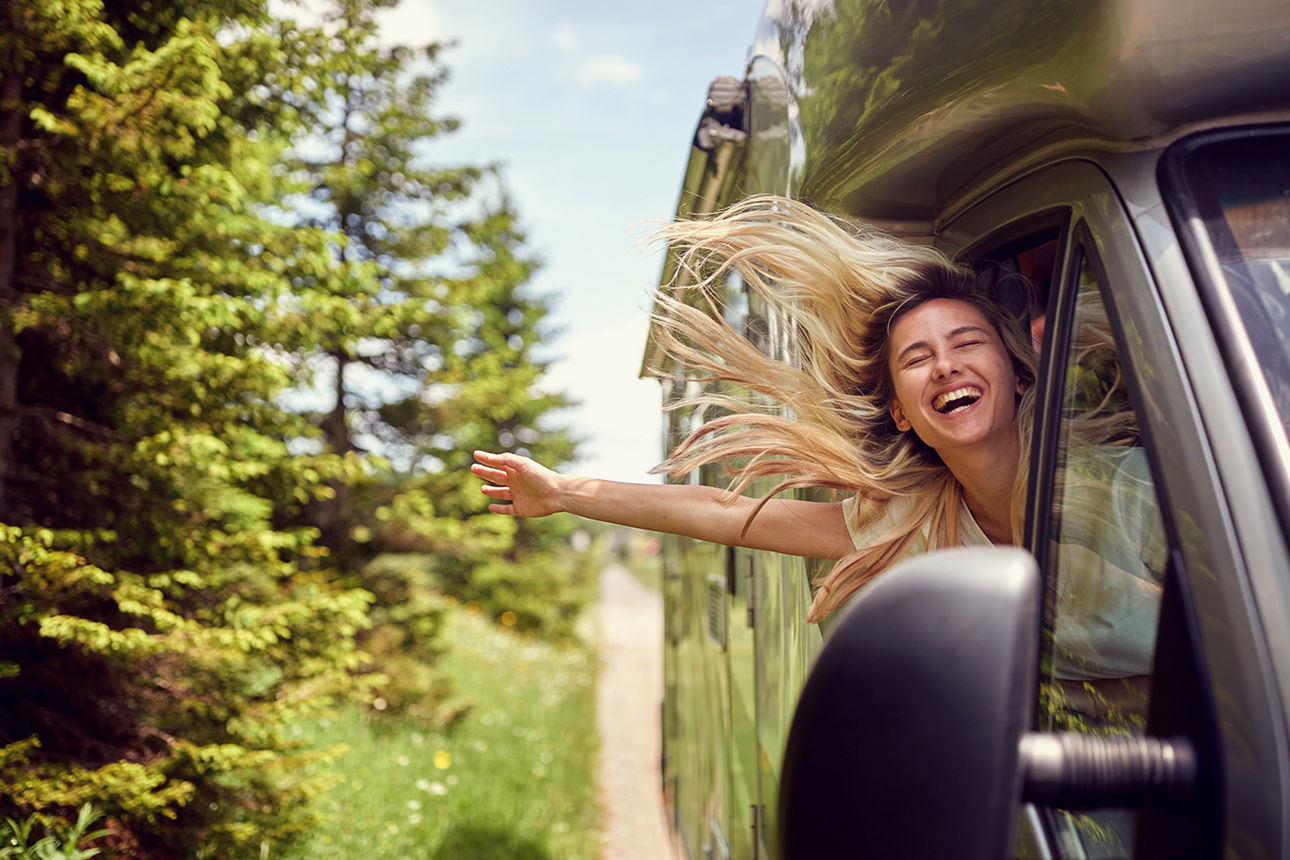 Frau lehnt sich lachend während der Fahrt aus dem Auto