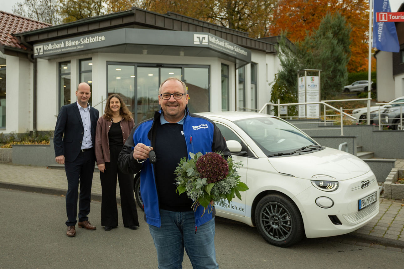 Autogewinner Markus Pilch vor seinem Fiat 500 Elektro, im Hintergrund Vertreter der VerbundVolksbank OWL 