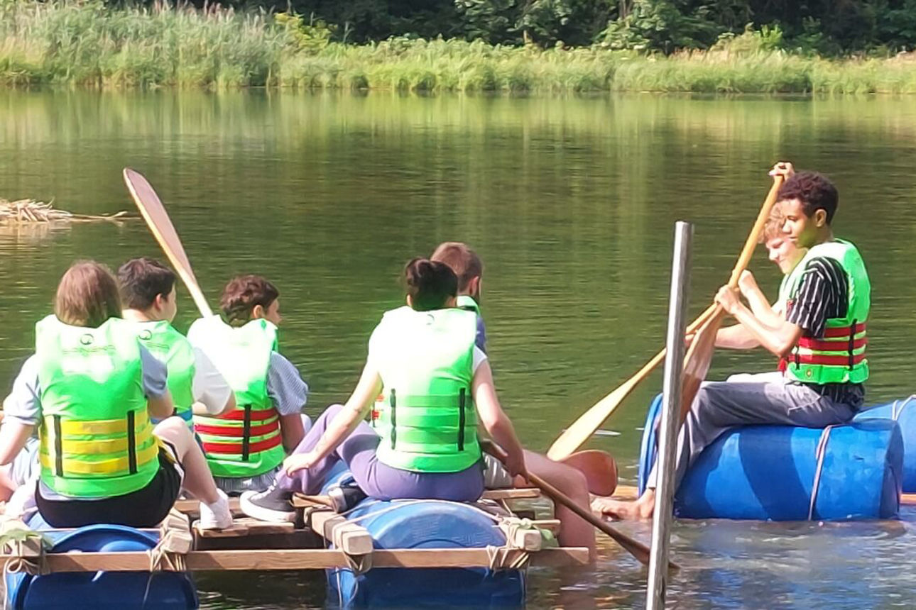 Unsere Azubis sitzen auf einem selbst gebauten Floß und paddeln auf der Iller