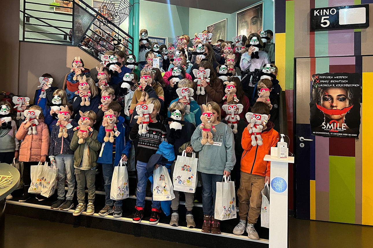 Teilnehmerkinder mit einem Kuscheltier vor dem Gesicht aufgestellt zu einem Gruppenbild auf einer Treppe