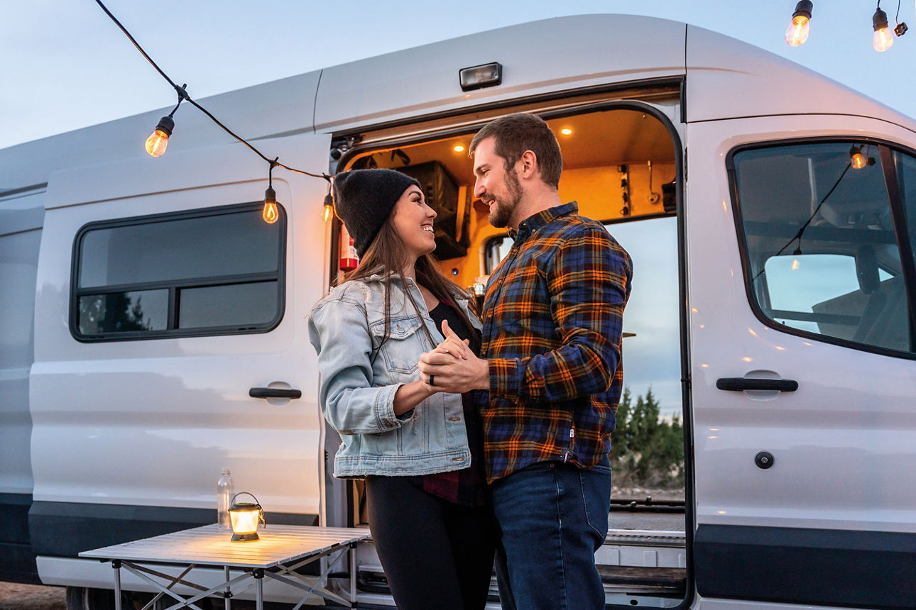 Junges Paar steht vor dem neuen Camper und schaut sich verliebt an