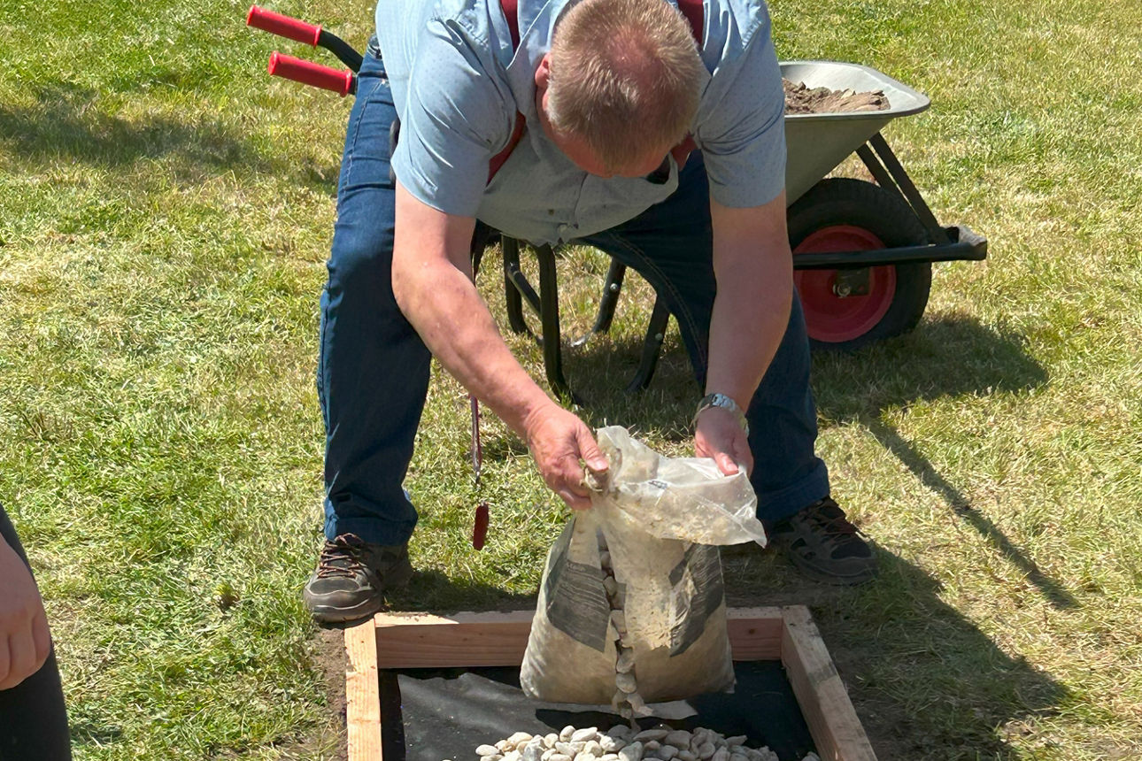 Ein Mann steht gebückt vor dem Barfußpfad und befüllt diesen mit Steinen.