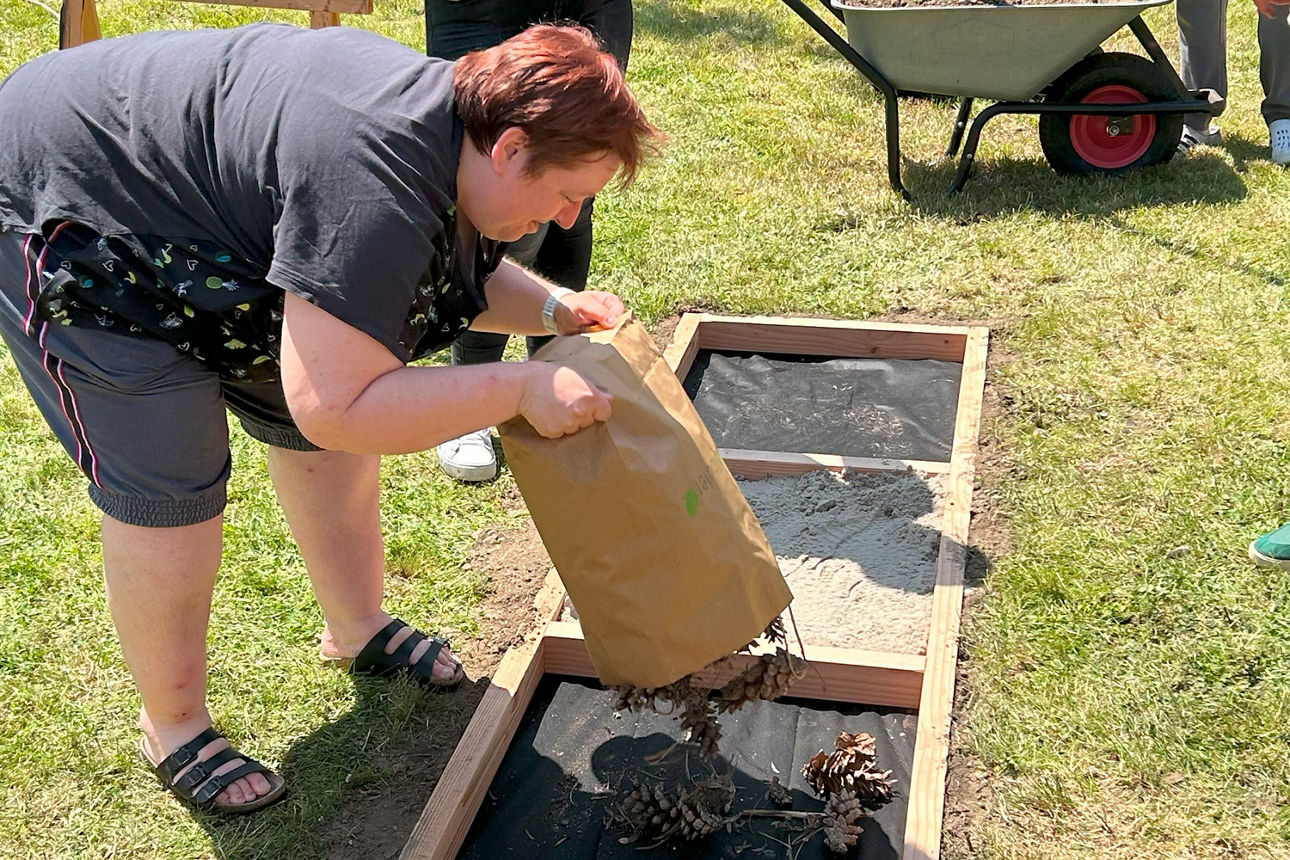 Eine Frau befüllt den Barfußpfad mit Tannenzapfen aus einer Tüte. 