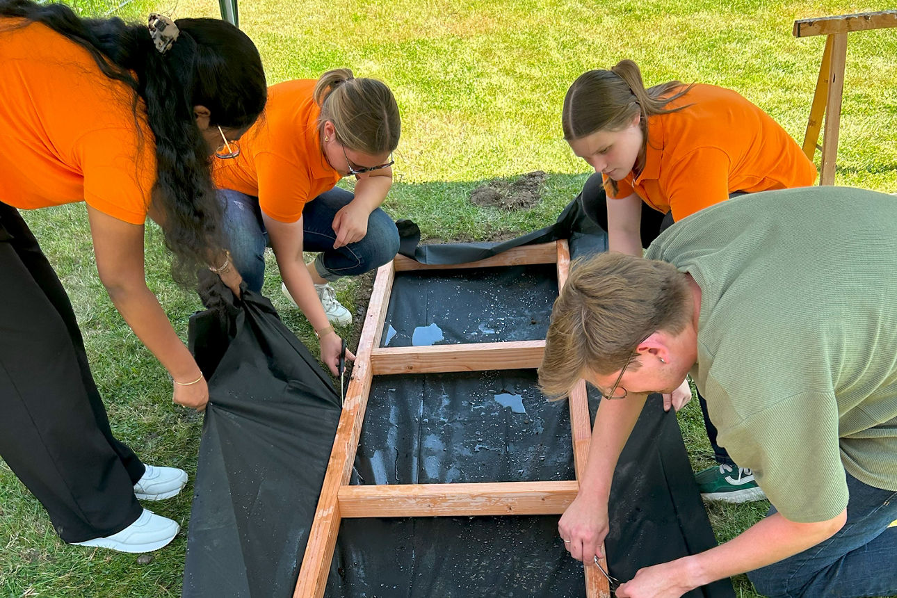 Vier Arbeiter hocken zusammen vor dem Holzgestell des Pfades und spannen eine Plane.
