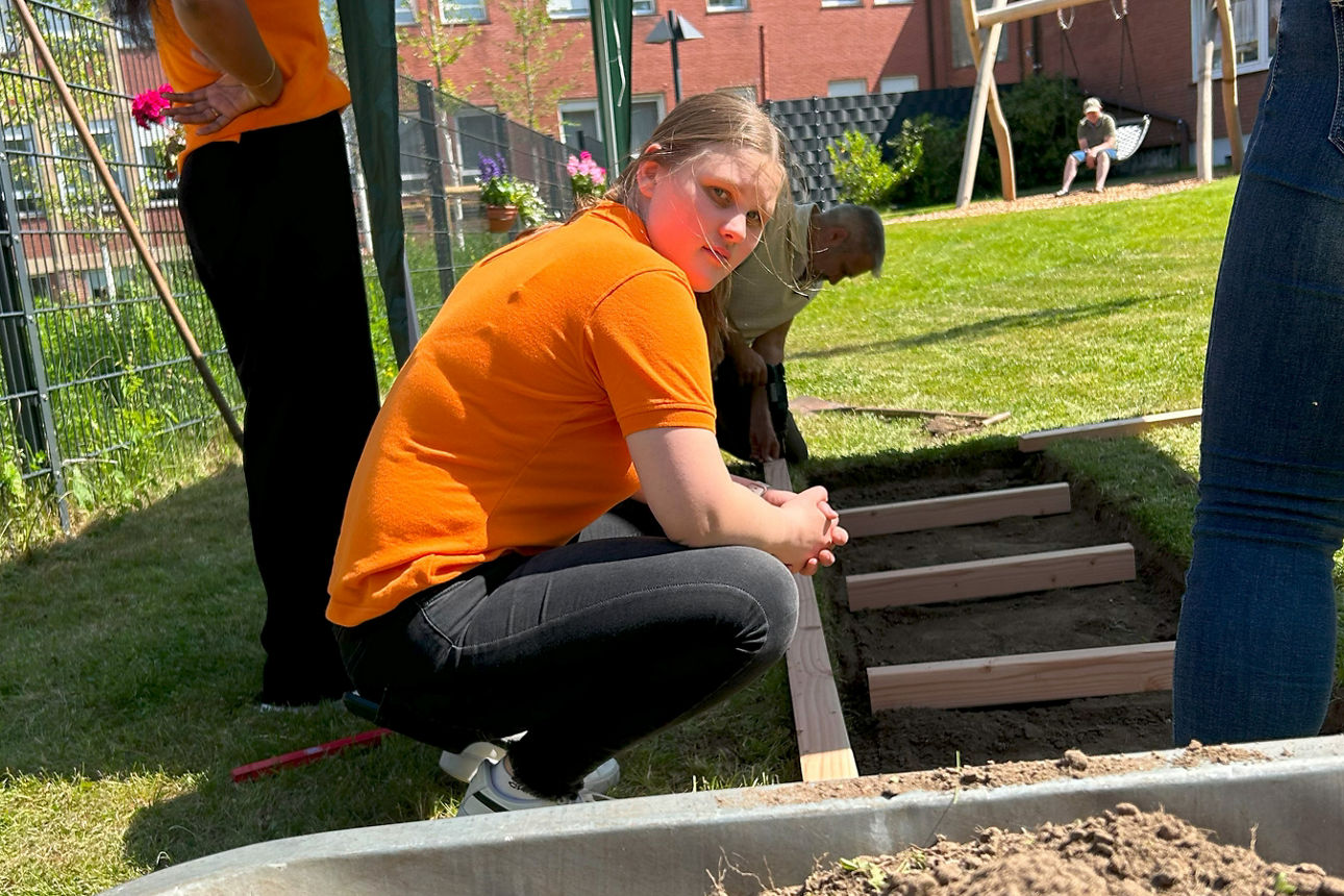 Eine Frau kniet hinter einer Schubkarre vor dem Grundgerüst des Barfußpfades zwischen drei Arbeiter*innen.