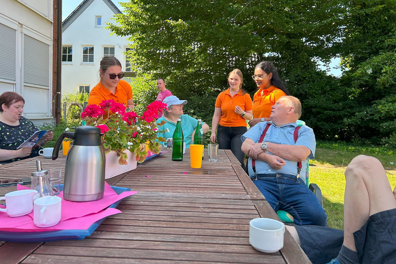 Eine Gruppe Menschen ist zusammen an einem Tisch und unterhält sich. 