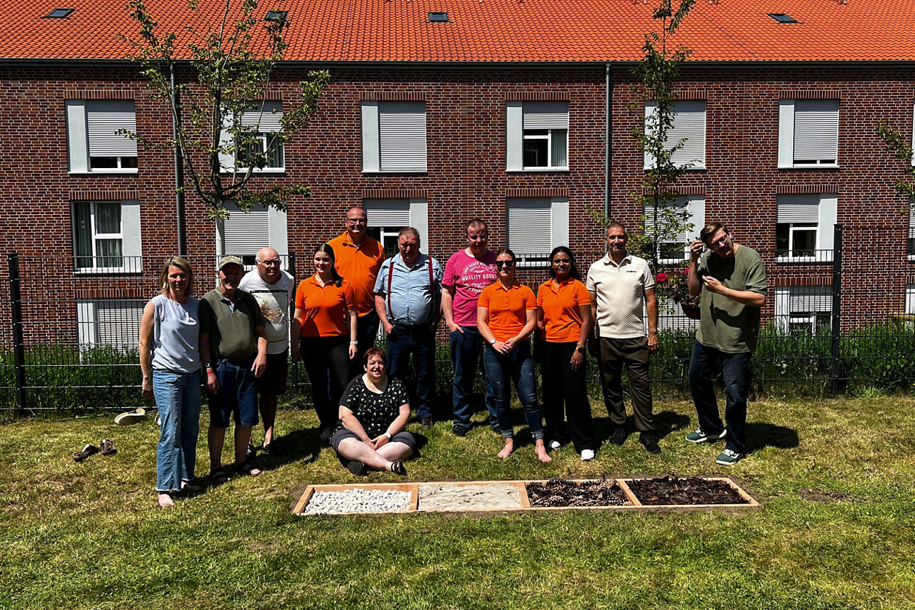 Eine Gruppe Menschen steht in einer Reihe vor einem Gebäude und einem Barfußpfad