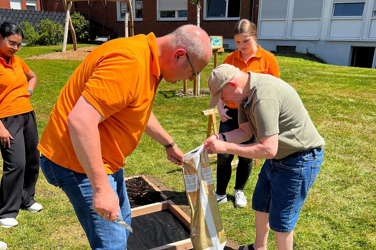 Zwei Personen befüllen zusammen den Barfußpfad. Zwei andere gucken zu. 
