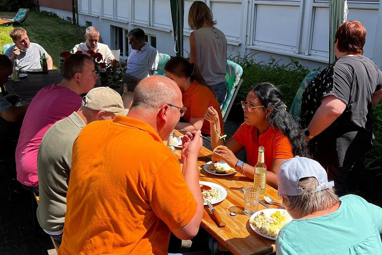Eine Gruppe Menschen sitzt zusammen am Tisch unter einem Pavillon und isst gemeinsam