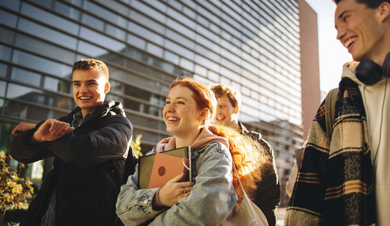 Mehrere Schüler:innen laufen lächelnd bei Sonnenschein an einem Gebäude vorbei