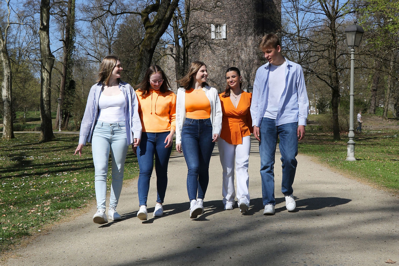 Eine Gruppe von fünf Auszubildenden der VR Bank Main-Kinzig-Büdingen geht  gemeinsam im Park spazieren und lacht miteinander.