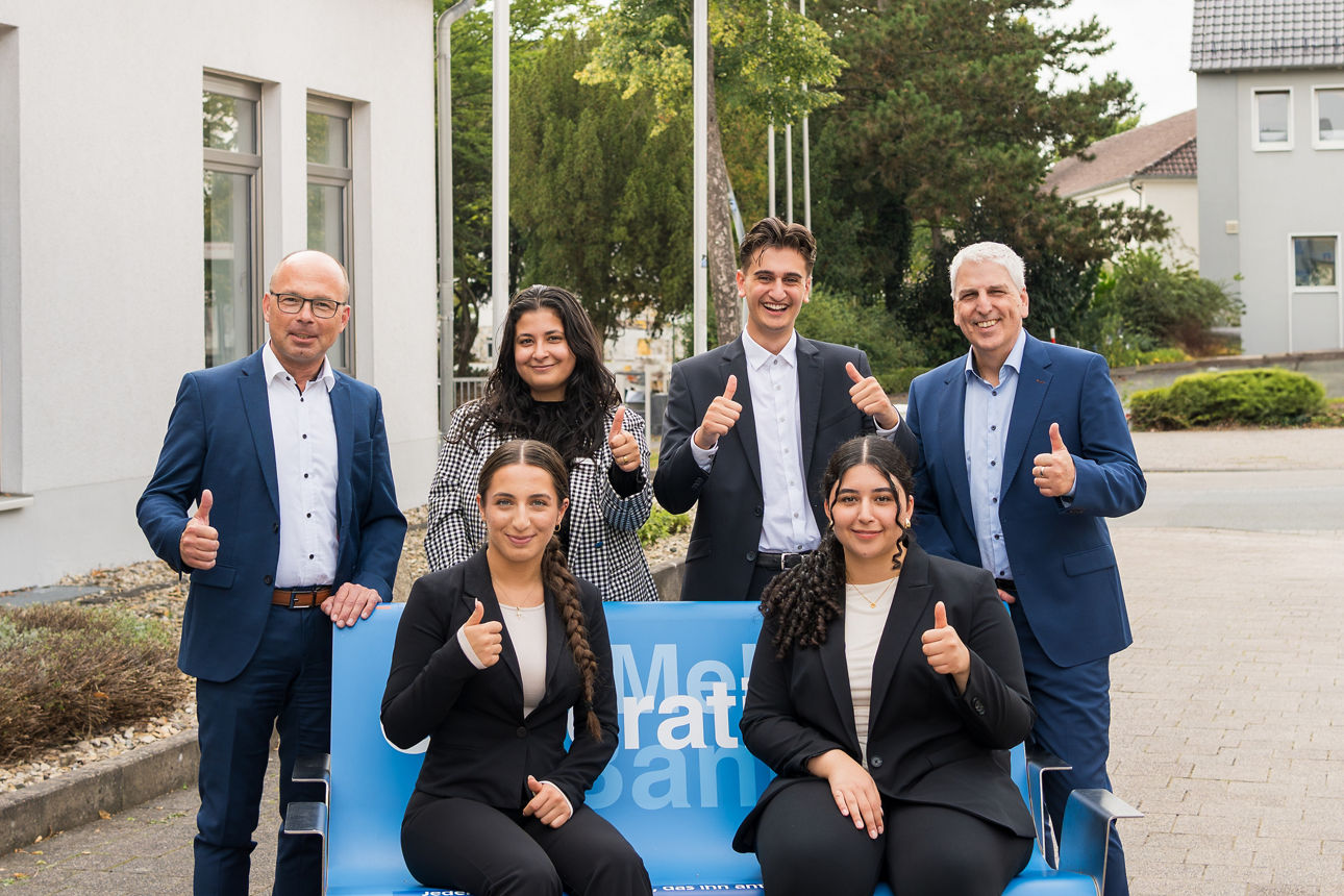 Eine Gruppe junger Menschen sitzend und stehend um eine blauen Bank versammelt.