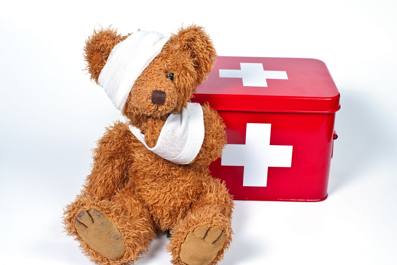 Teddybär mit Verband sitzt vor rotem Erste Hilfe Kasten