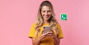Eine junge Frau mit langen blonden Haaren lächelt, während sie auf ihr Smartphone schaut