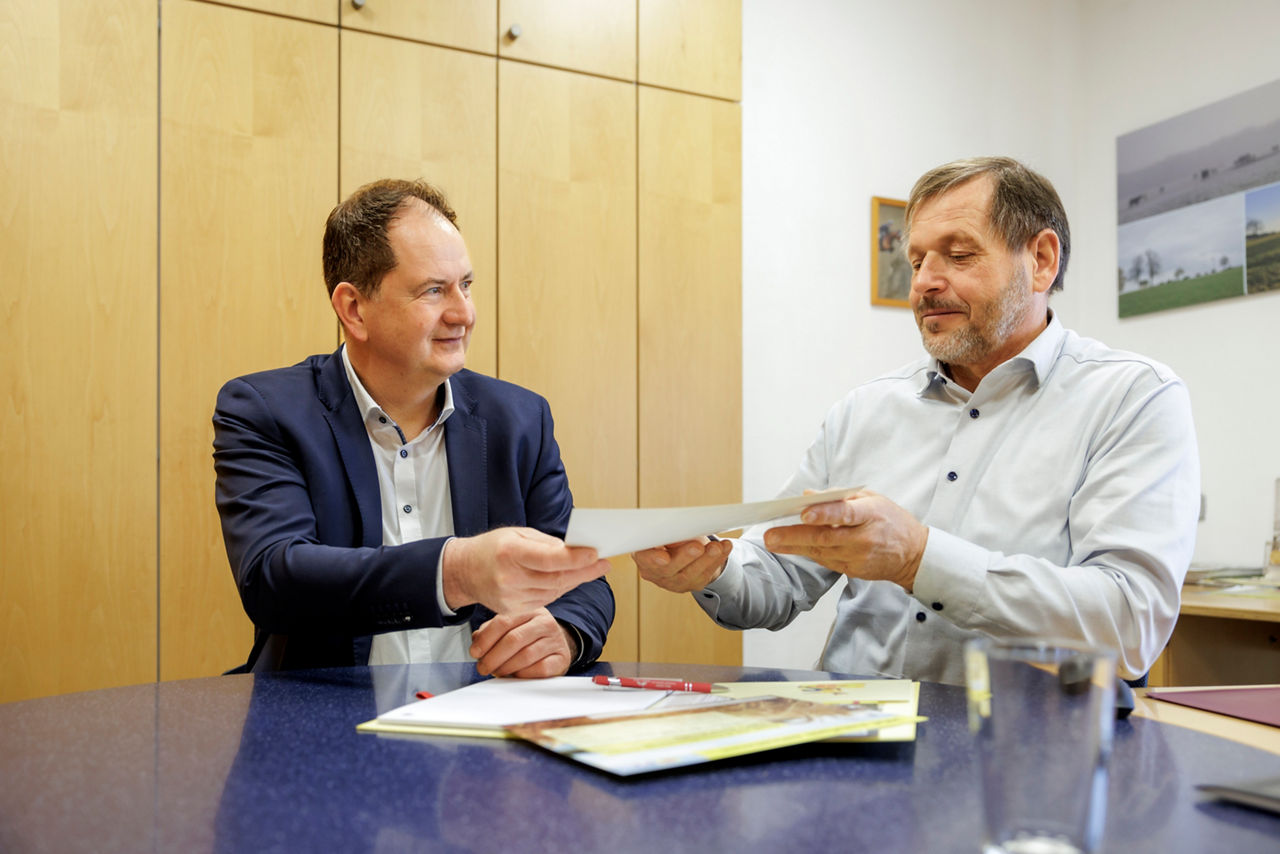 Zwei Berater im Hemd und Anzug sitzen im Bankbüro und tauschen Bankdokumente aus.